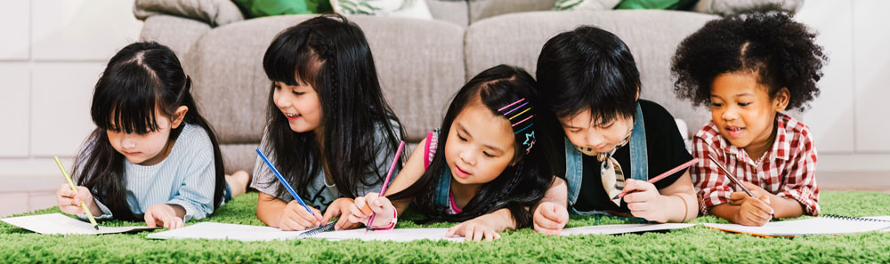 Short I CVC sentence dictation featured image of 5 students writing while lying on a green rug.