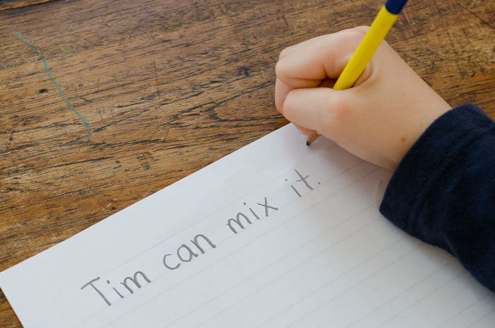 A child writes the dictated sentence Tim can mix it.