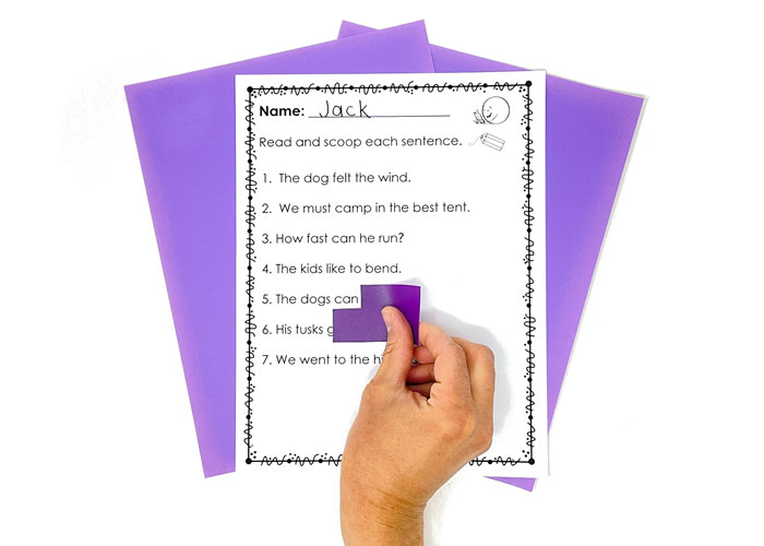 A hand using a slider with a corner cut out to read sentences on a page.